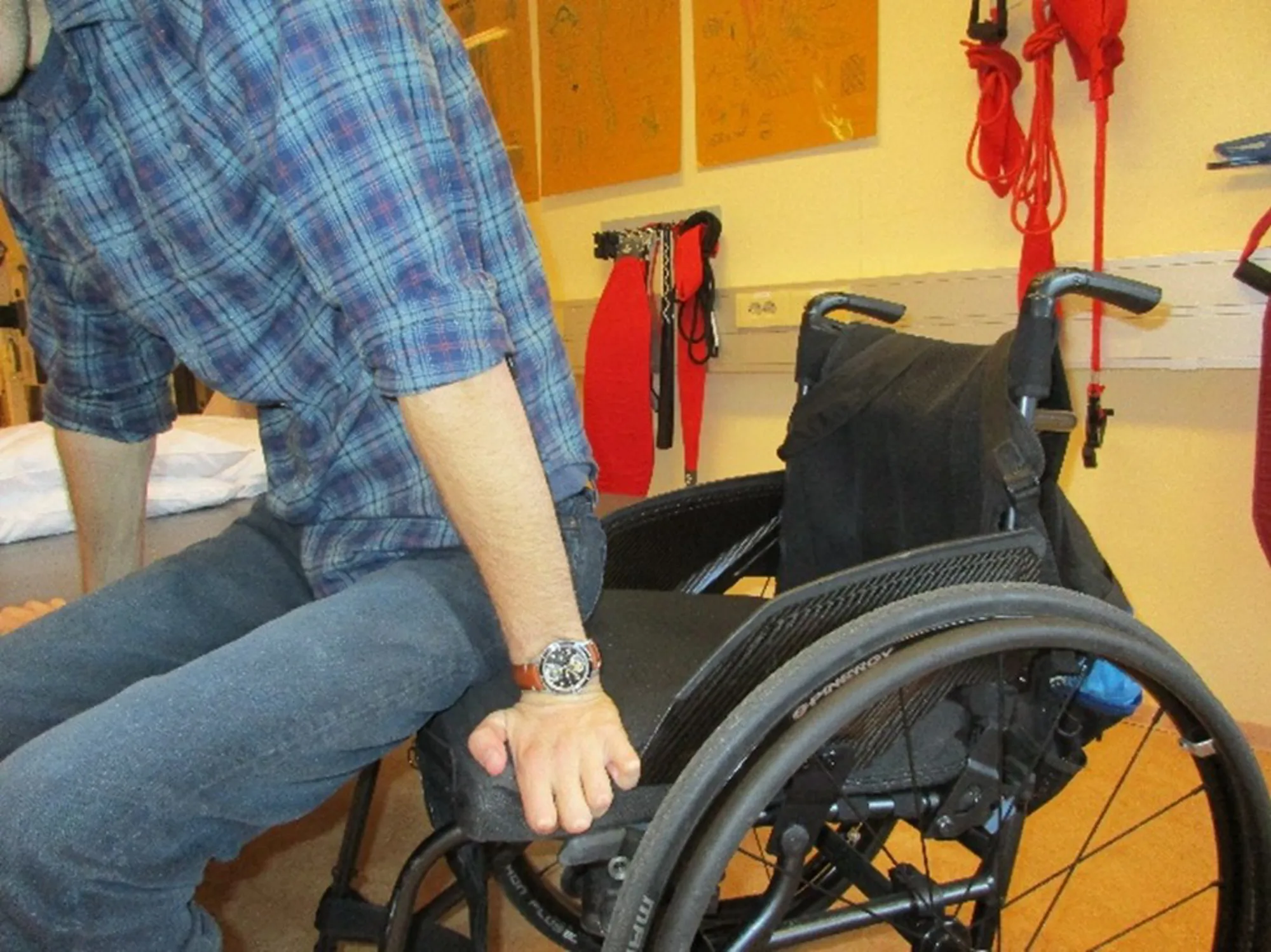 En person som sitter i rullestol og bruker hendene til å støtte seg med for å reise seg.