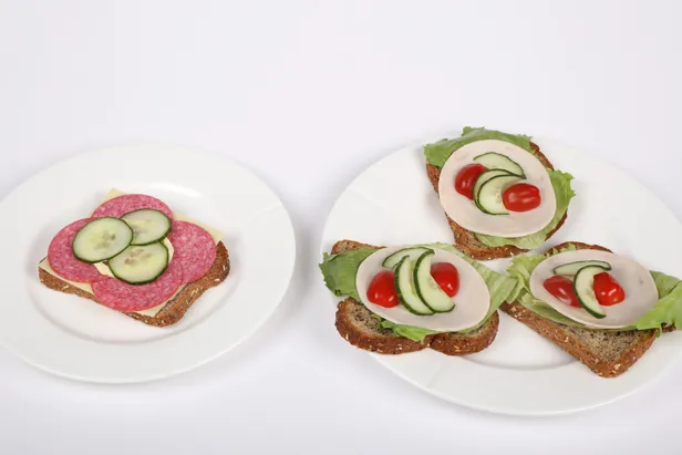 Et fat med en brødskive med majones, salami og agurk, samt et fat med tre brødskiver med salatblad, kalkunpålegg, tomater og agurkskiver.