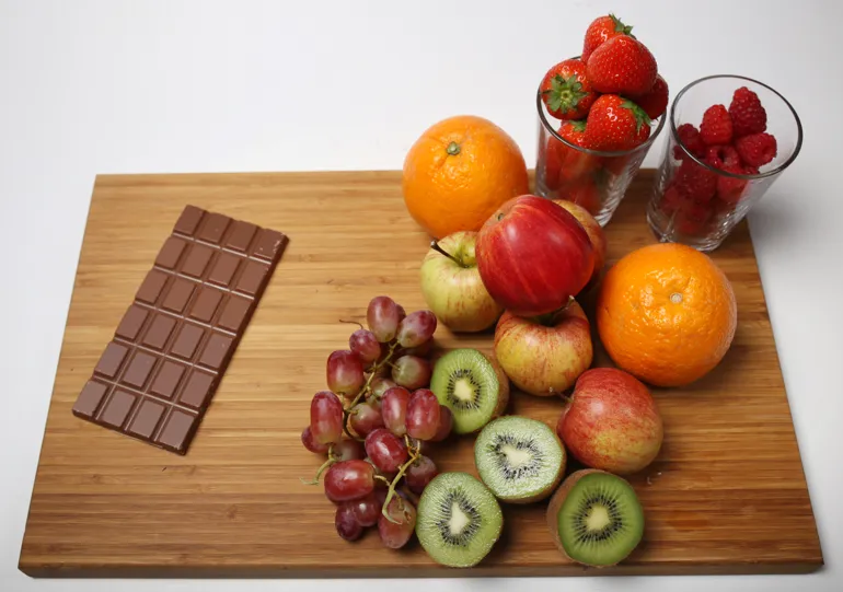 Et brett med en åpnet sjokoladeplate, druer, kiwi, epler, appelsiner, jordbær og bringebær