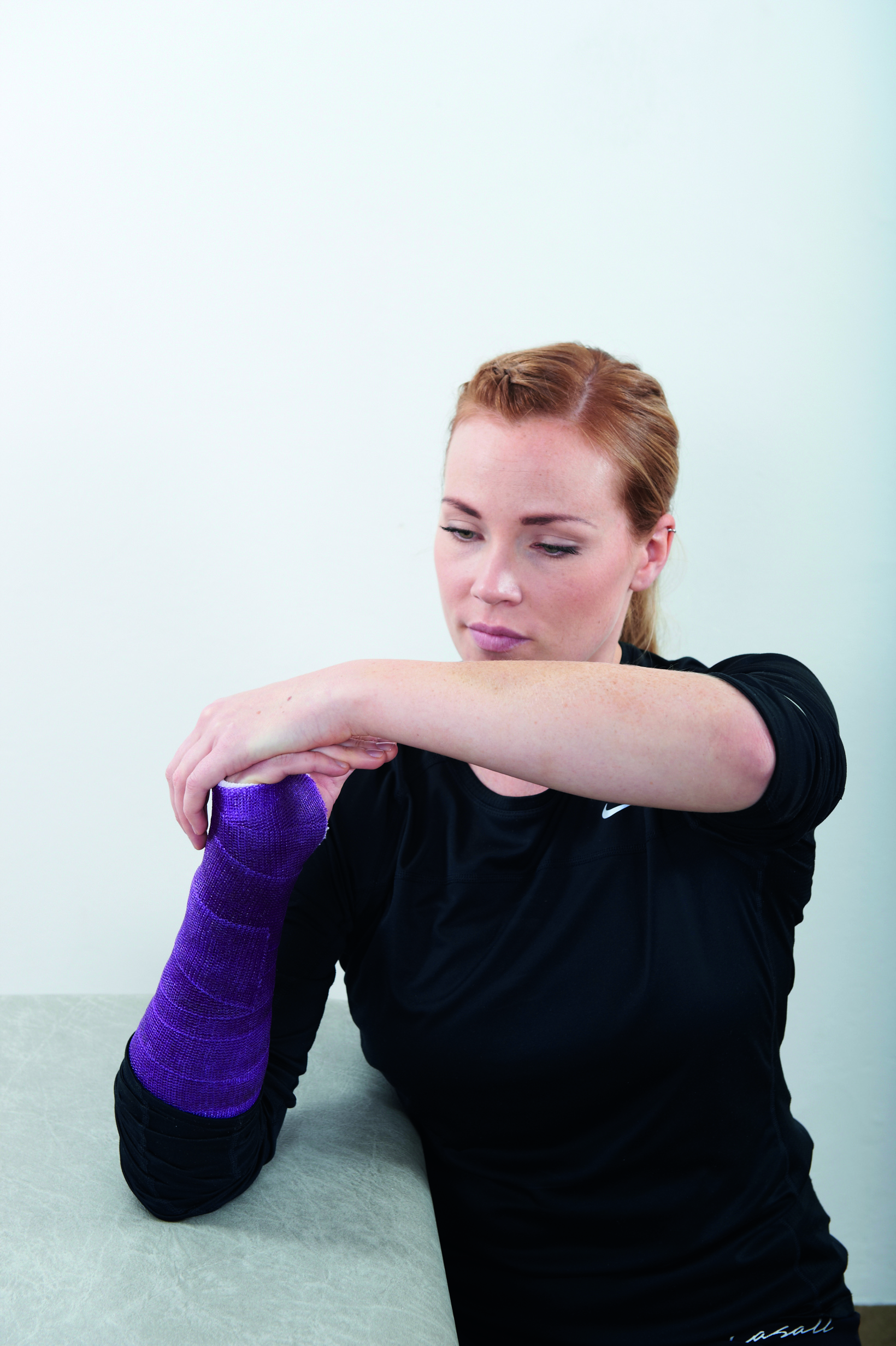Dame med gipset arm viser hvordan man tøyer knokene.