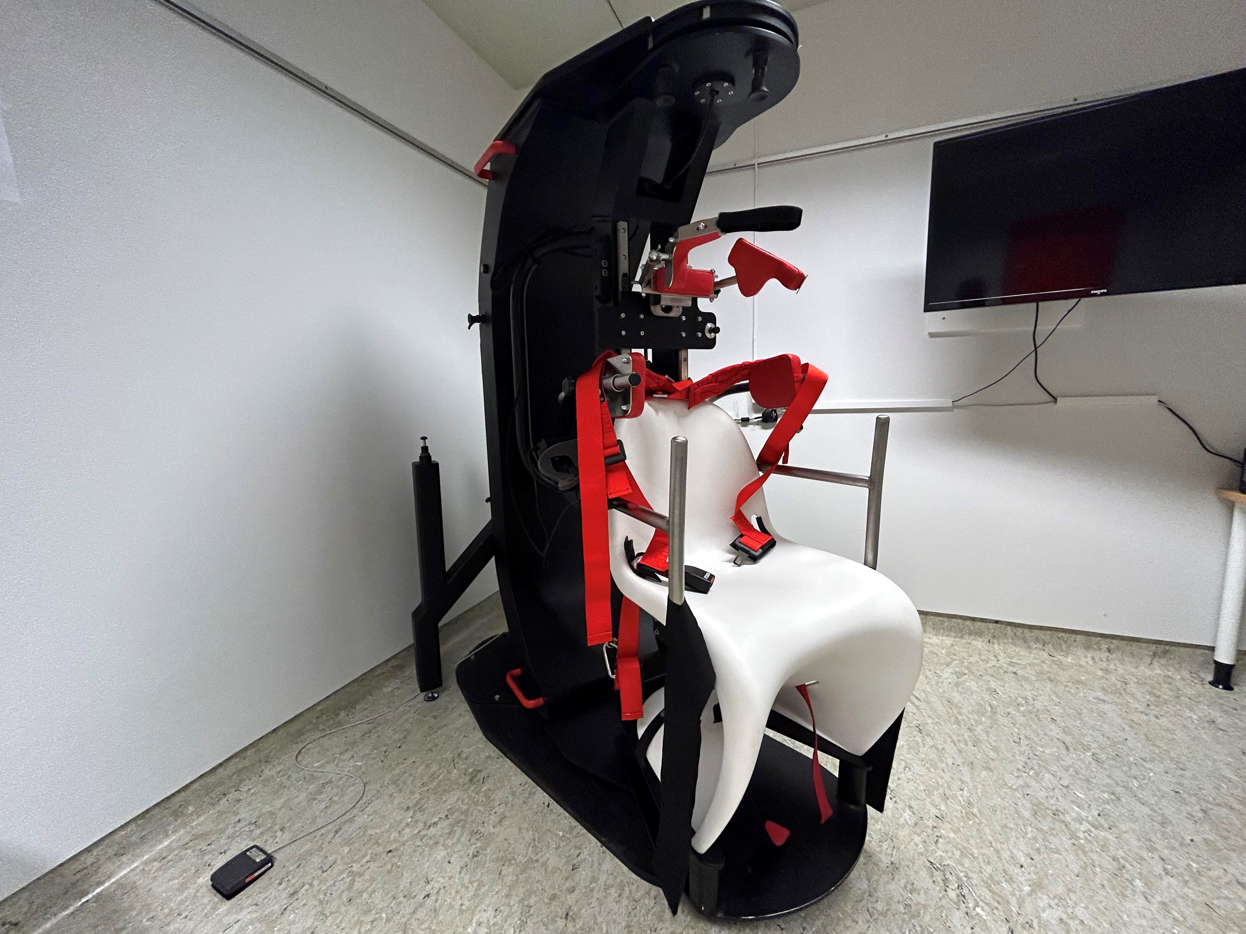 Undersøkelsesrom med rotasjonsstol og TV-skjerm på vegg.