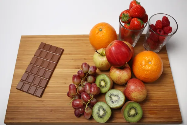 Et brett med en åpnet sjokoladeplate, druer, kiwi, epler, appelsiner, jordbær og bringebær
