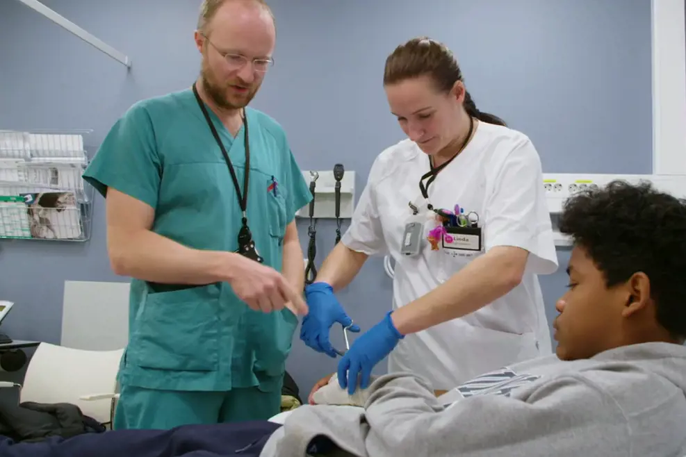 Ortoped og sykepleier klipper opp gipsen til pasienten, en ung gutt med mørkt hår