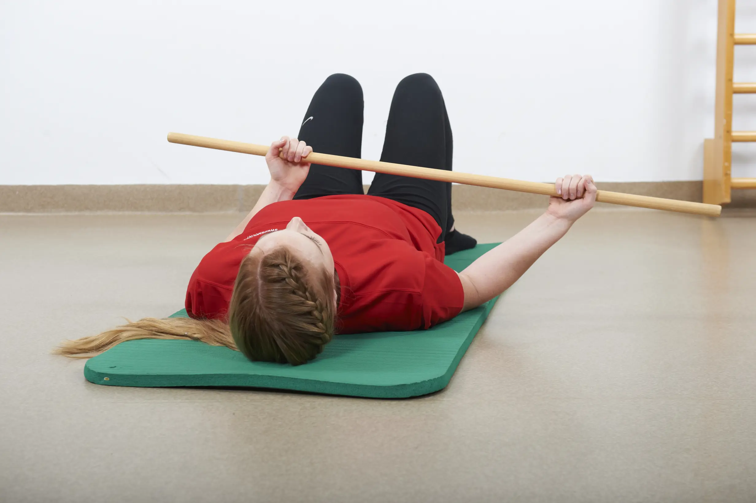 Ligg på ryggen med en stokk, langkost eller lignende. La albuen hvile mot underlaget. Rotér armen utover ved hjelp av den friske