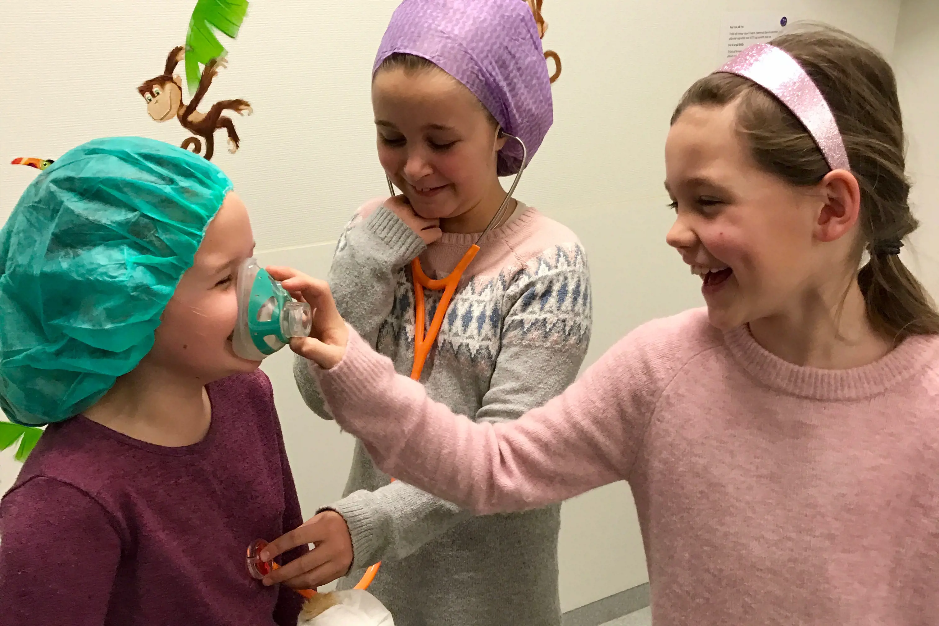 Tre jenter leiker med oksygenmaske og stetoskop. 