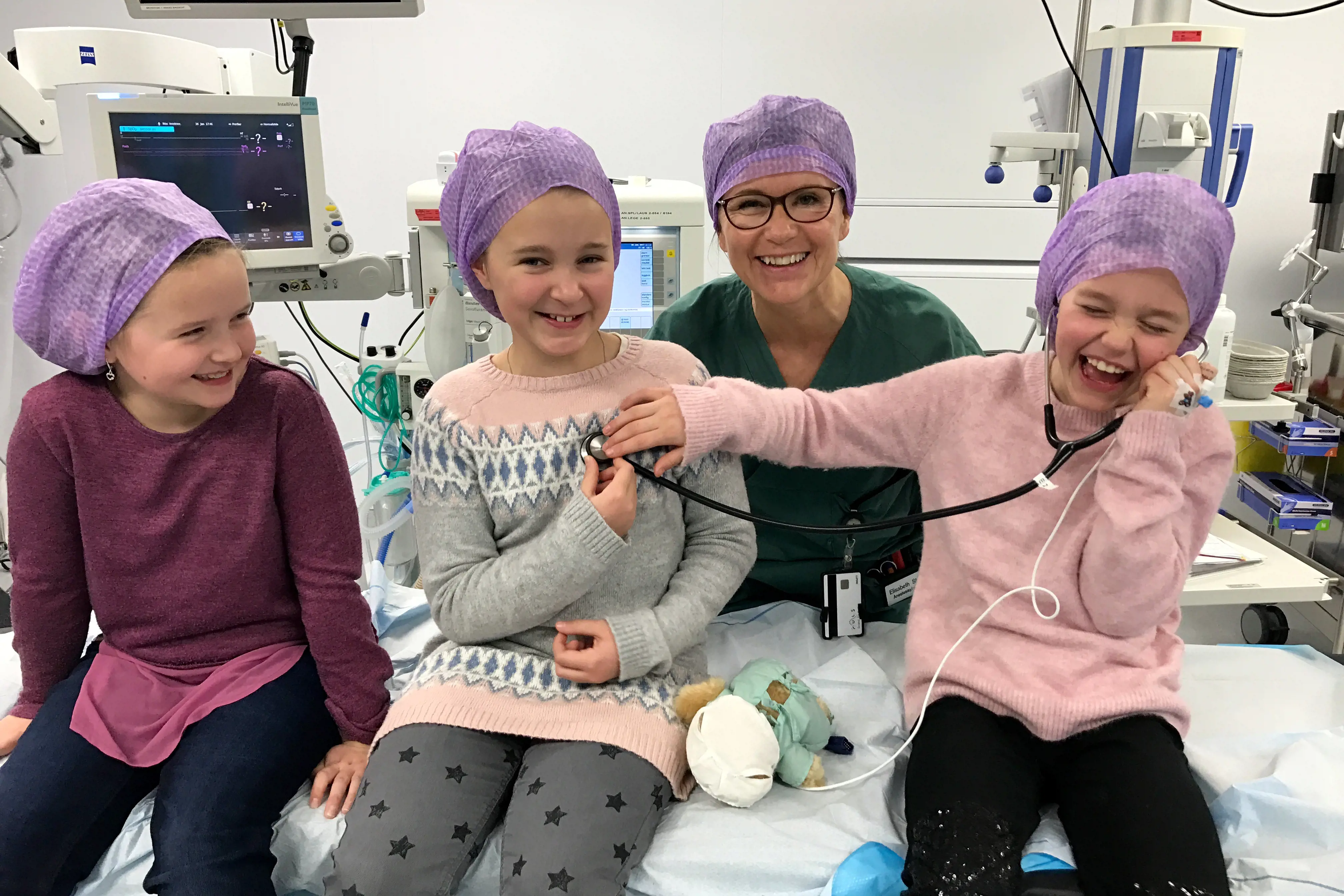 Tre jenter og ein anestesisjukepleiar på operasjonsstova. Her får dei lytte på kvarandre med eit ekte stetoskop. 