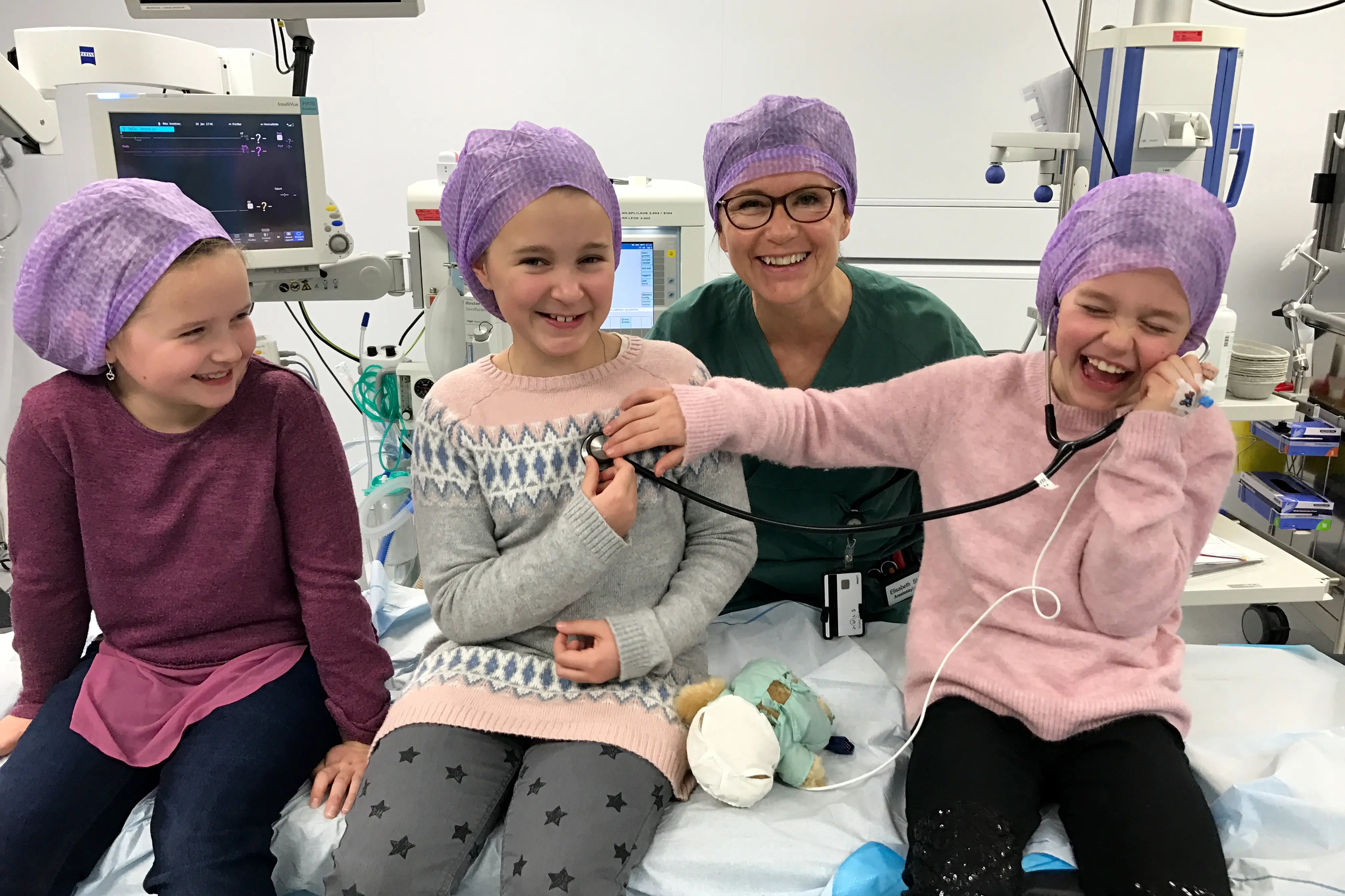 Tre jenter og ein anestesisjukepleiar på operasjonsstova. Her får dei lytte på kvarandre med eit ekte stetoskop.