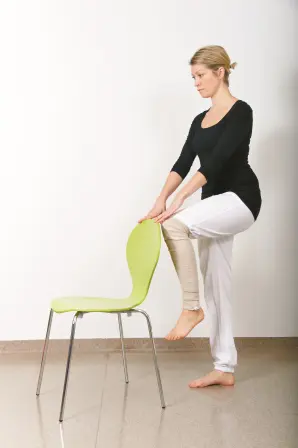 Dame holder i en stol mens hun løfter det ene benet