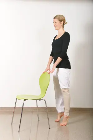 Dame holder i en stol mens hun står på tærne