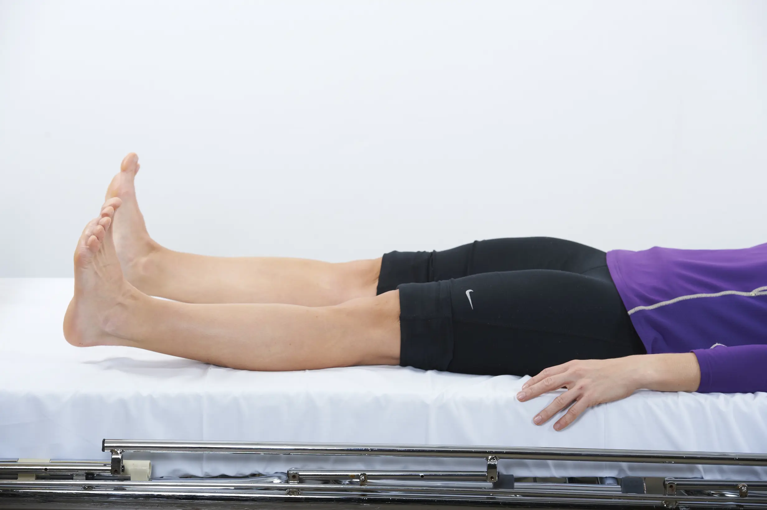 Dame som ligger på en benk mens hun strammer lårmusklene slik at knehasene presses mot underlaget