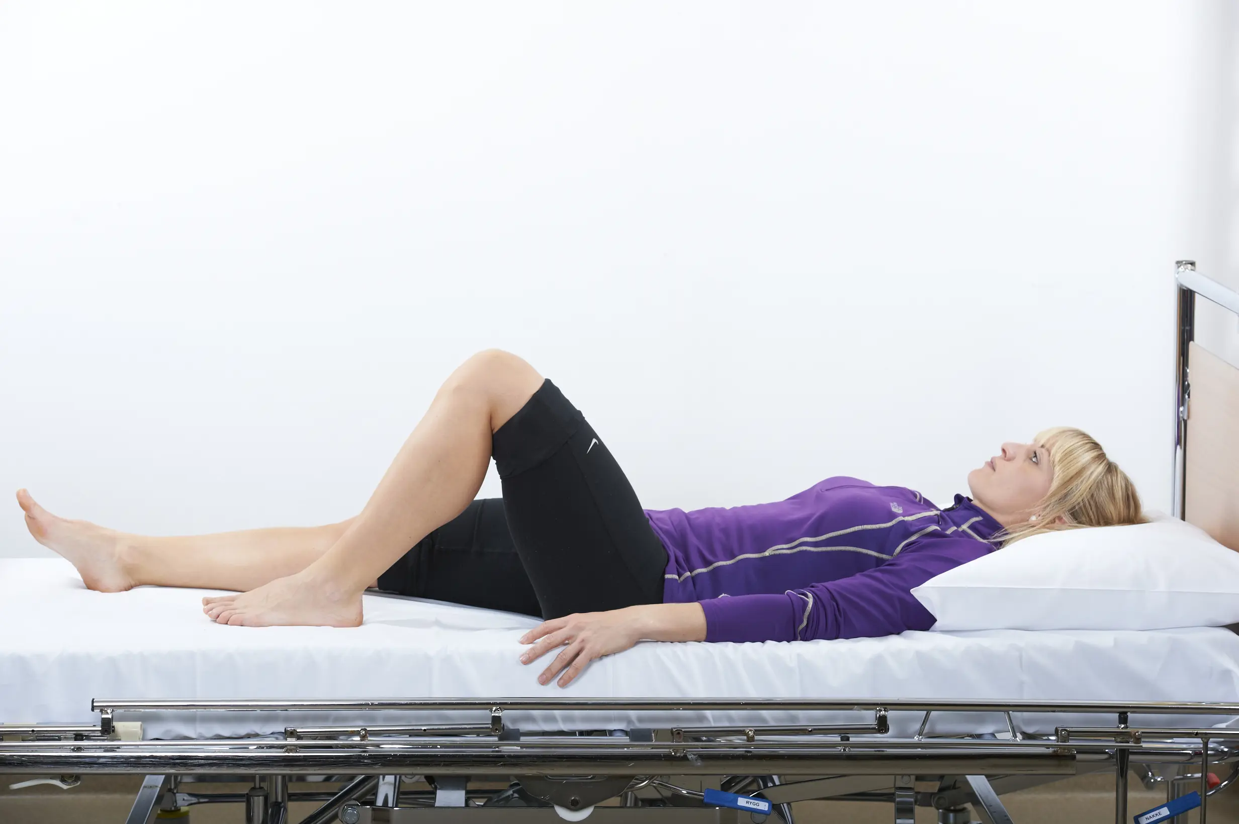 Dame ligger på en sykehusseng med det ene benet bøyd