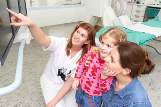 Bilde av radiograf, barn og mamma. Radiografen peker opp på en skjerm og de to andre ser opp på skjermen.